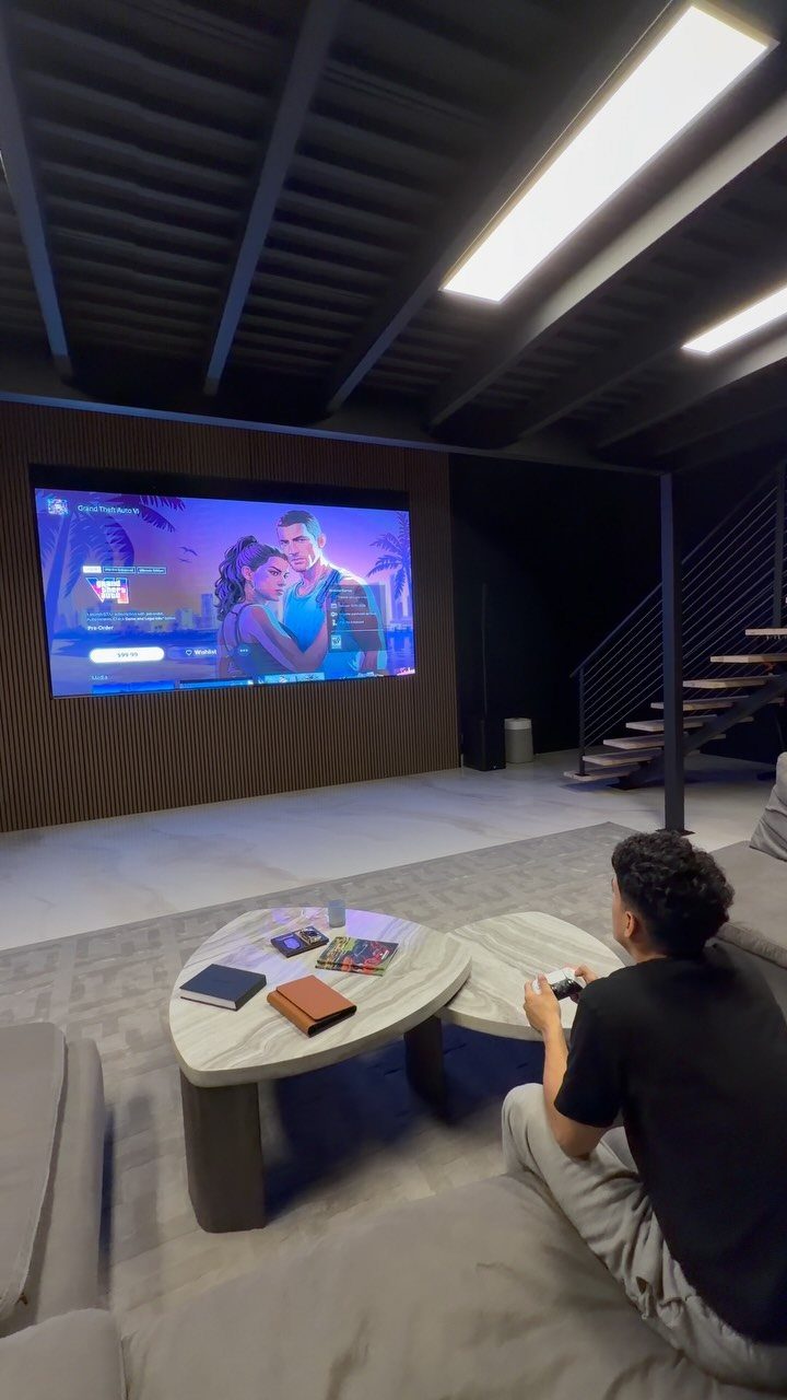 Person sitting on a sofa watching a large movie screen in a modern media room.