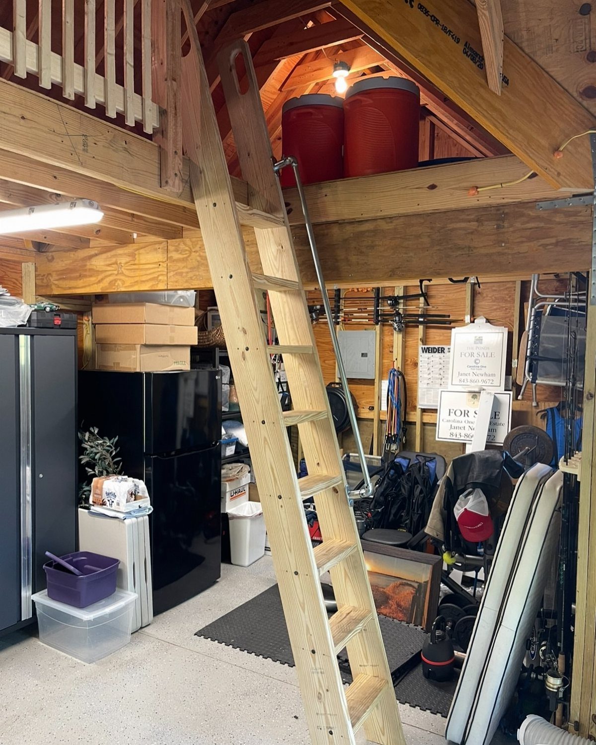 Wooden ladder leading to a loft storage area with two large red containers in a garage.