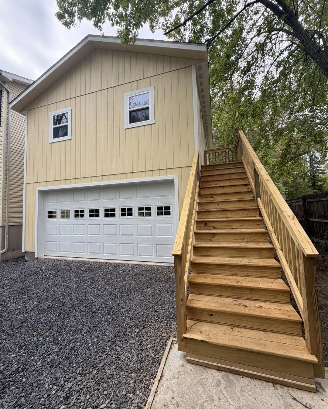 A tan two-story garage with a white door and wooden stairs leading to the upper level.