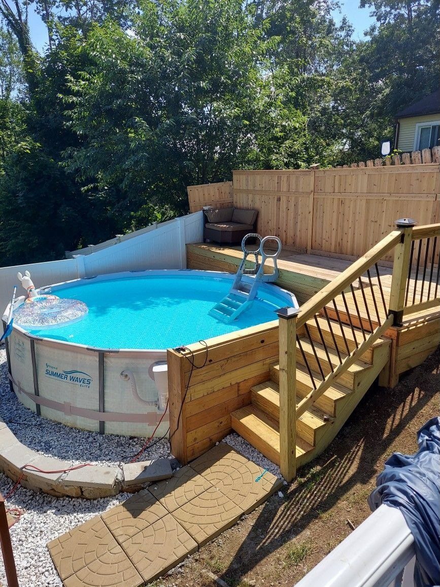 An above ground pool surrounded by a multi-level wooden deck with stairs and a seating area.