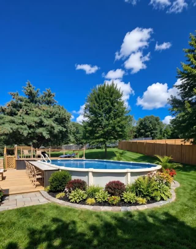 An above ground pool with a wooden deck attached to one side in a green backyard.