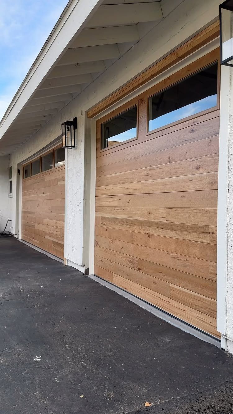 American House Garage Door: 7 Styles for Better Curb Appeal 5 Two modern wooden garage doors with horizontal planks installed on a white house exterior.