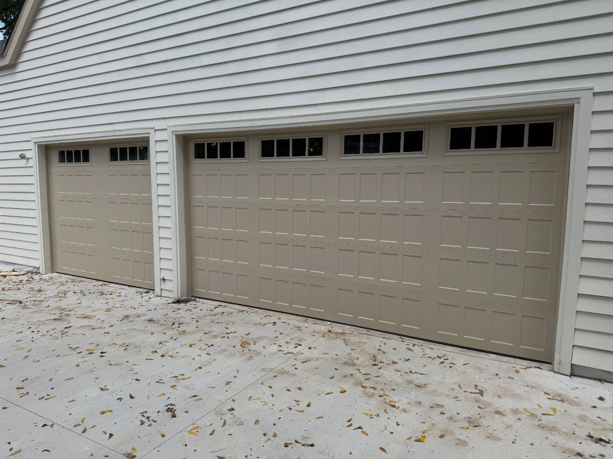 American House Garage Door: 7 Styles for Better Curb Appeal 2 Beige raised panel garage doors with windows installed on a white sided house.