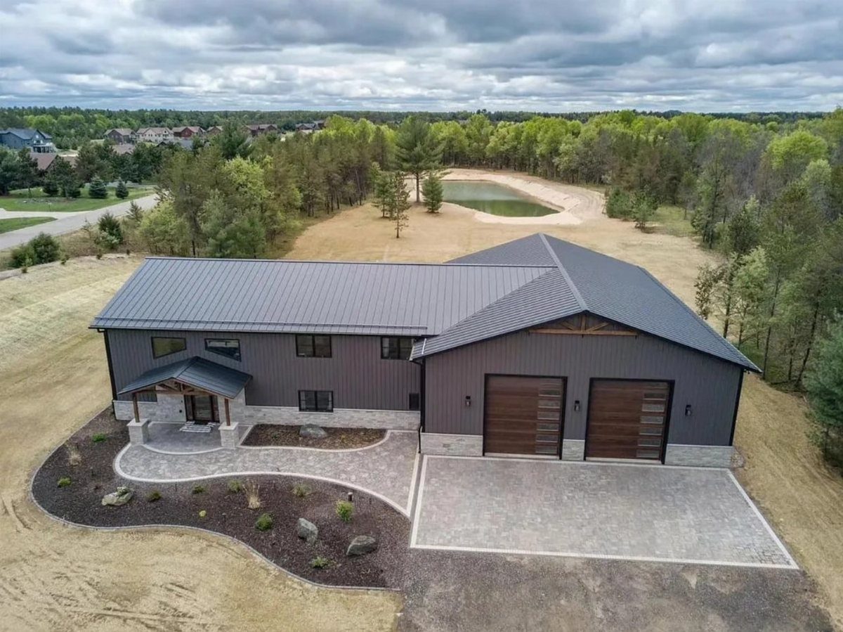 Aerial view of a modern black barndominium with a dark metal roof and wooden garage doors.