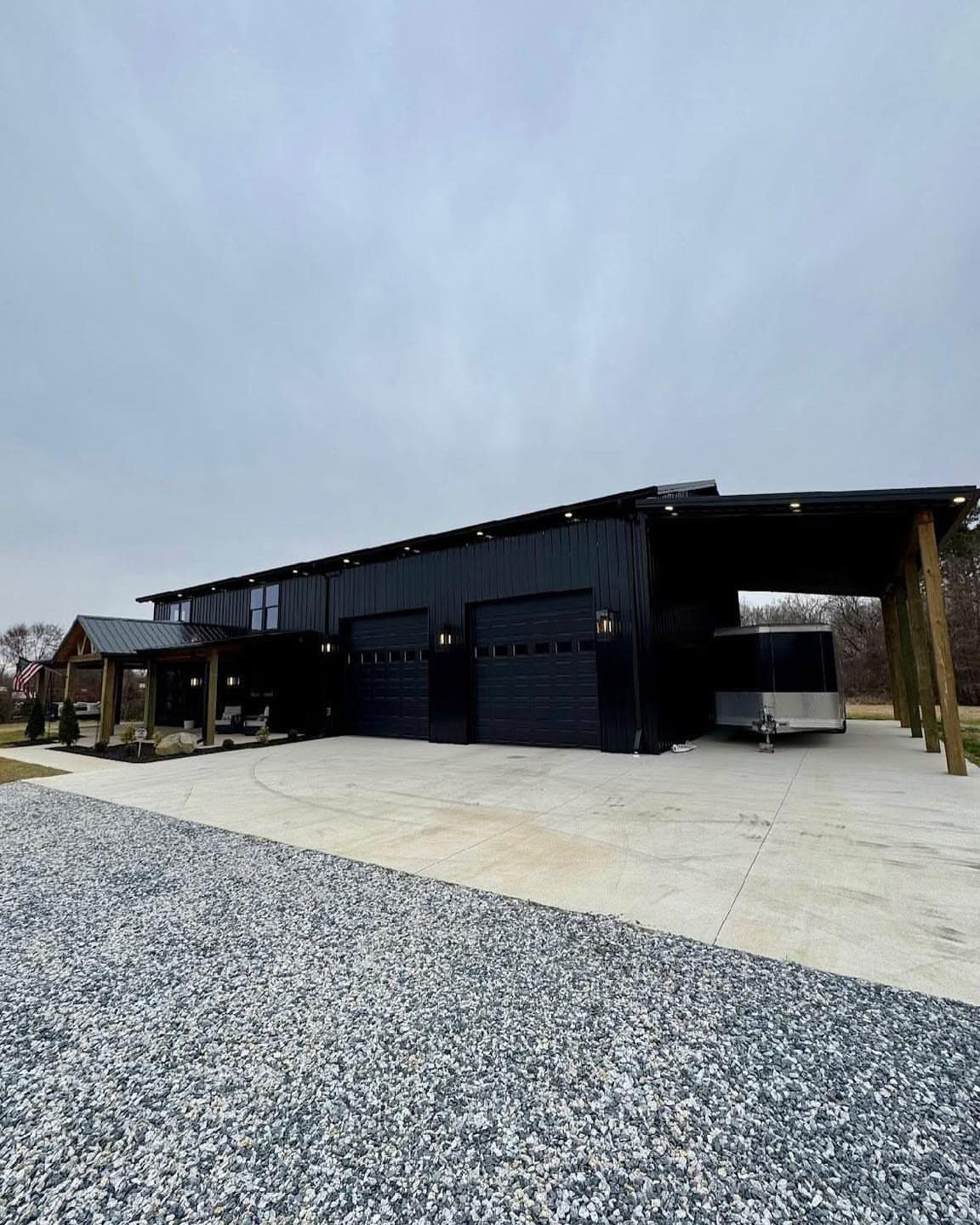 A large black metal pole barn with multiple garage doors and a covered porch area.