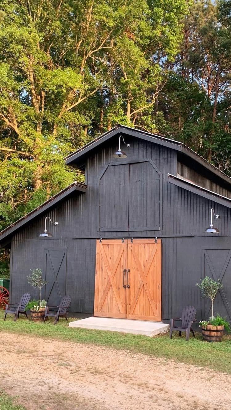 Black wooden pole barn with large natural wood doors and matte black vertical siding.