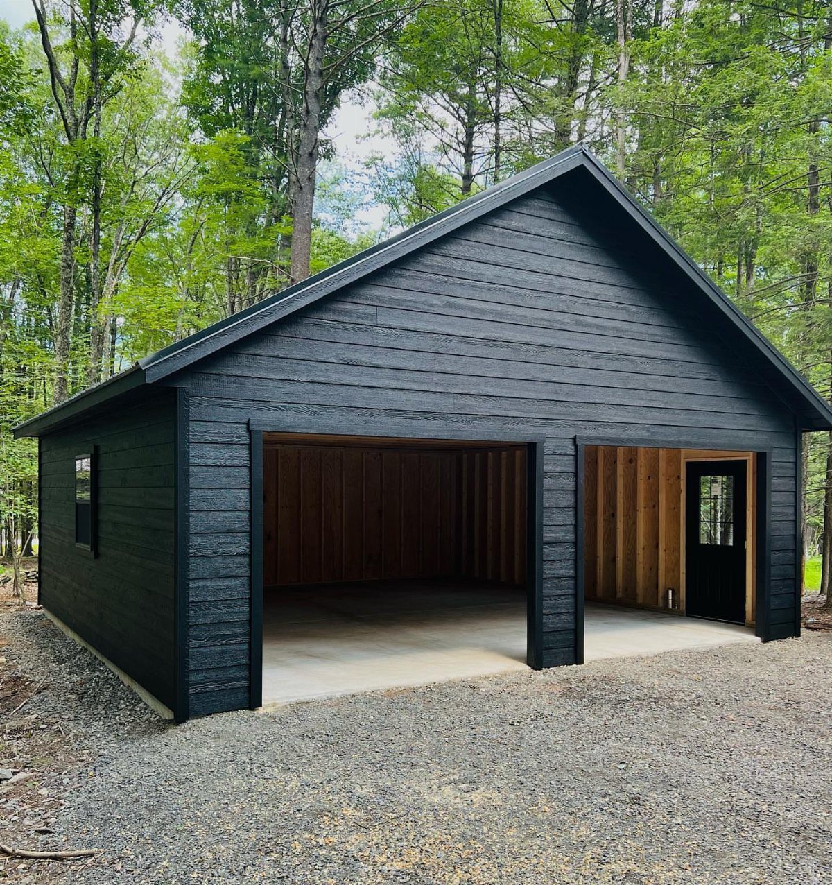Black pole barn garage with open bays revealing a wooden interior and concrete floor.