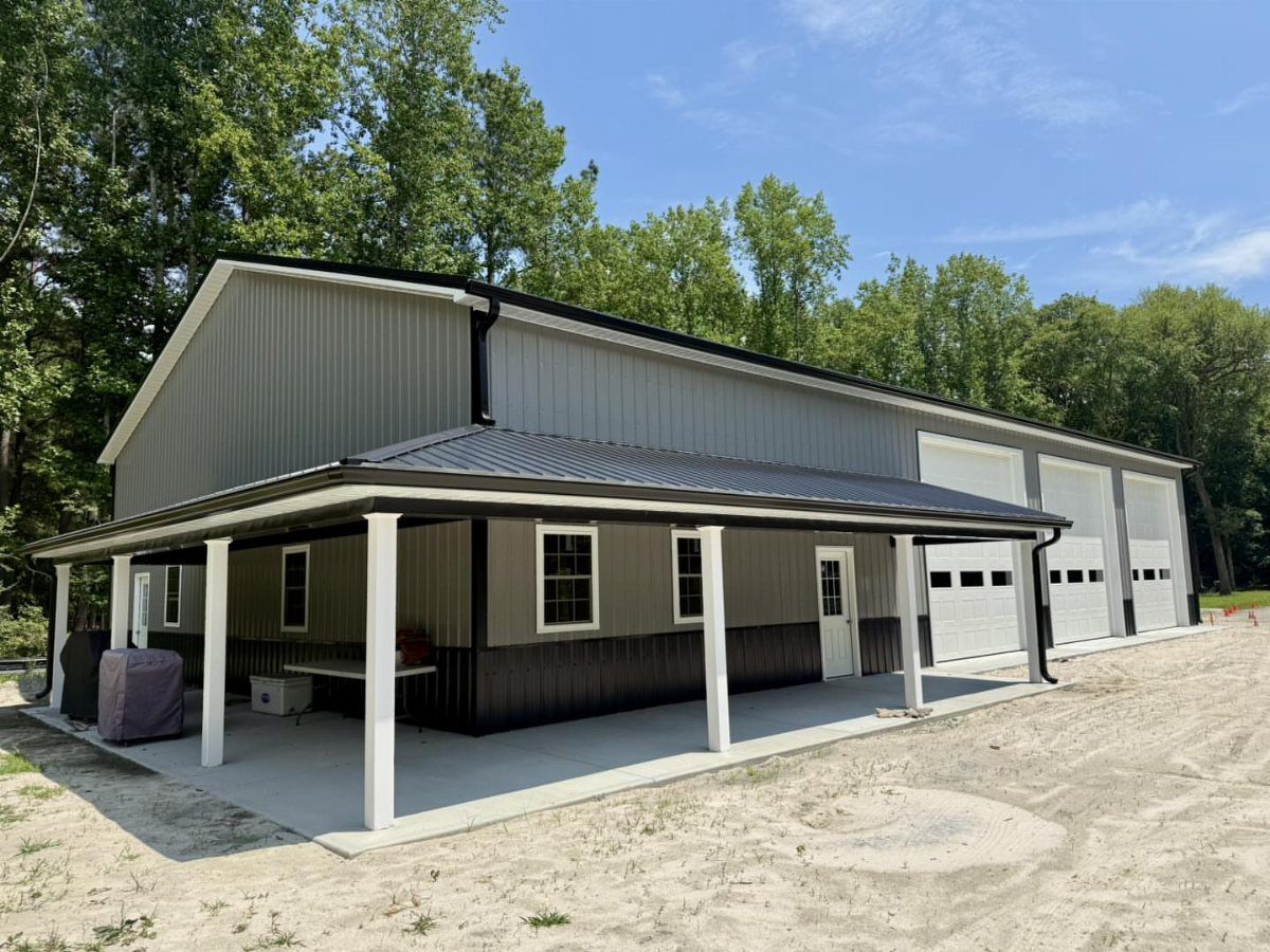 A large grey and black metal pole barn garage with a wide covered porch and white garage doors.