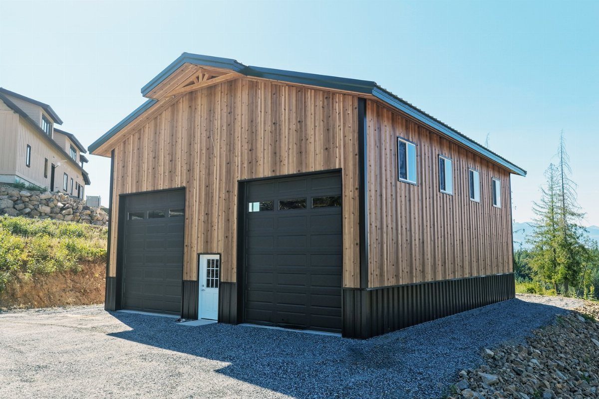 A wooden pole barn garage with black doors, a white door, and side windows.