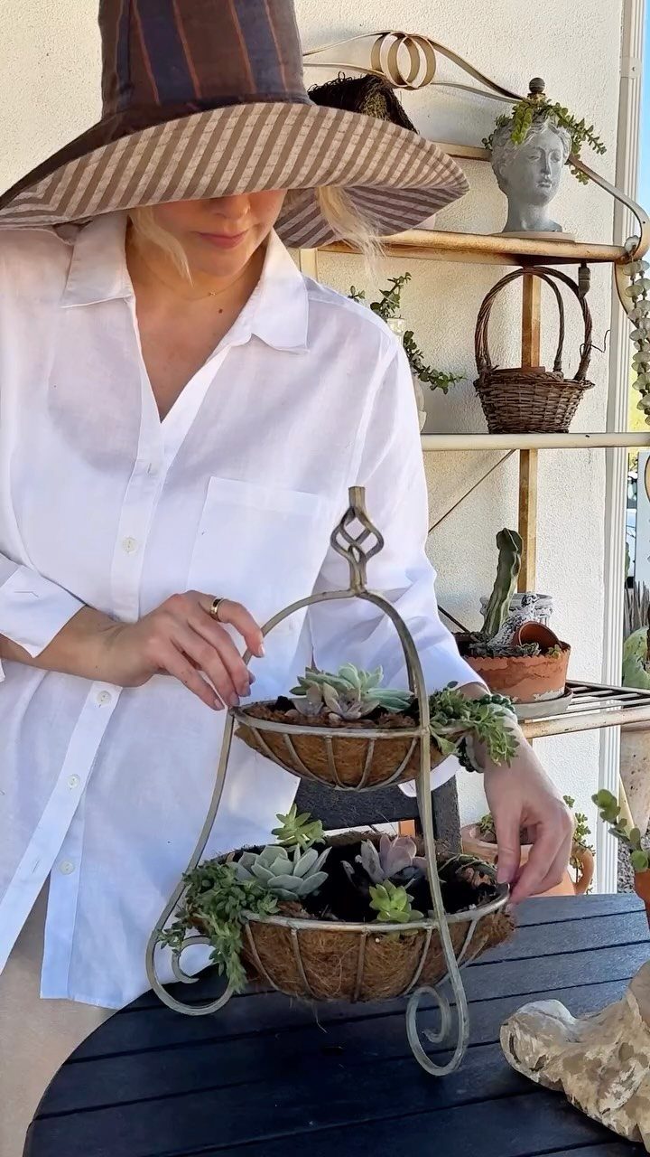 11 Cheap Container Gardening Ideas for Small Spaces 4 A woman tending to succulent plants in a tiered metal wire basket planter outdoors.