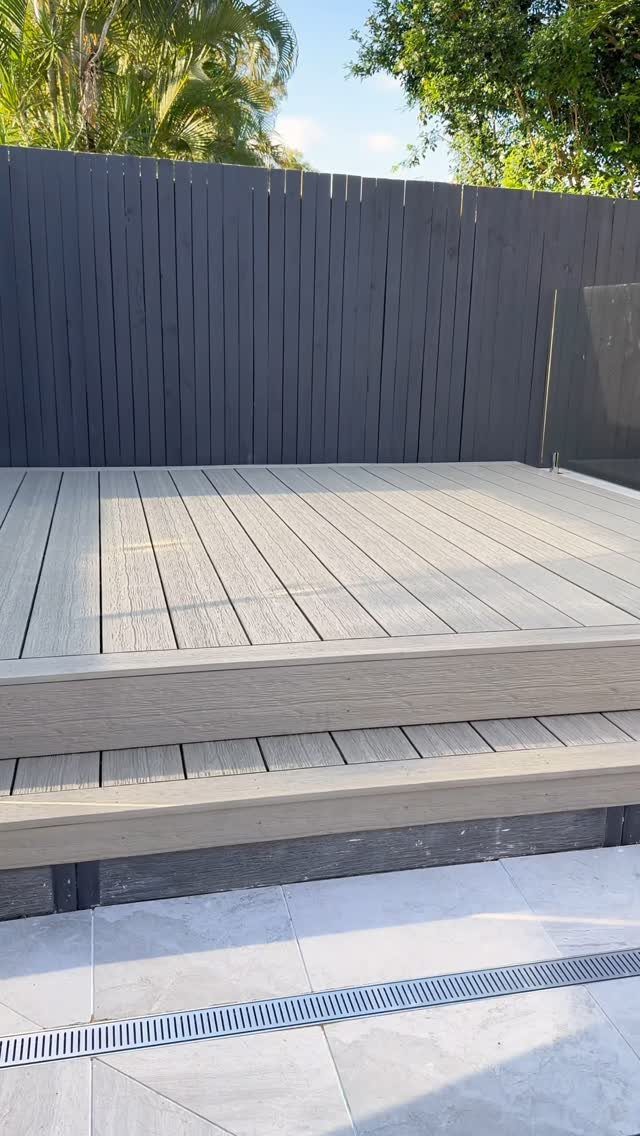Light grey composite wood deck with a raised step next to a dark grey fence.