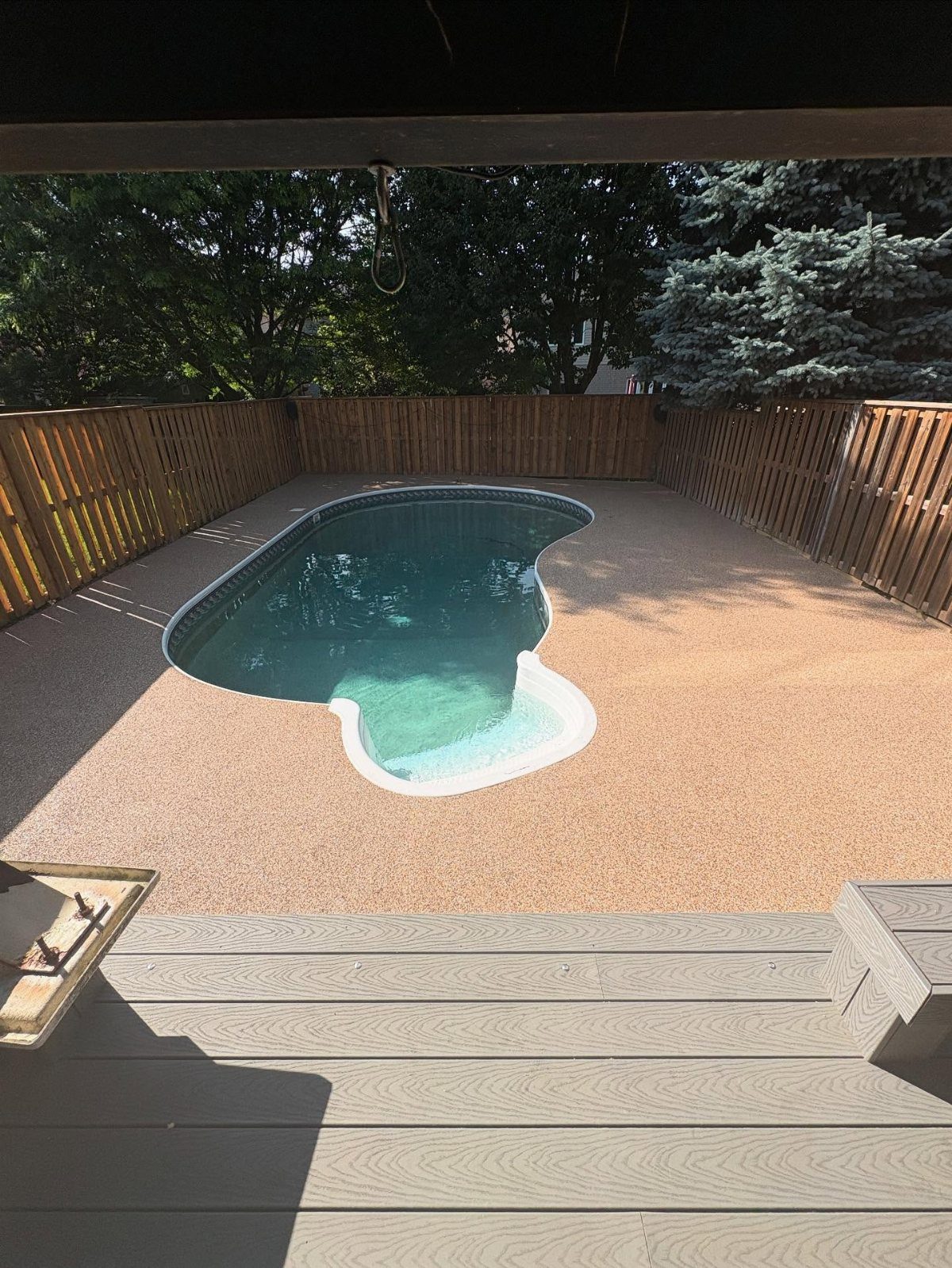An inground swimming pool with a tan pebble deck and a wooden privacy fence.