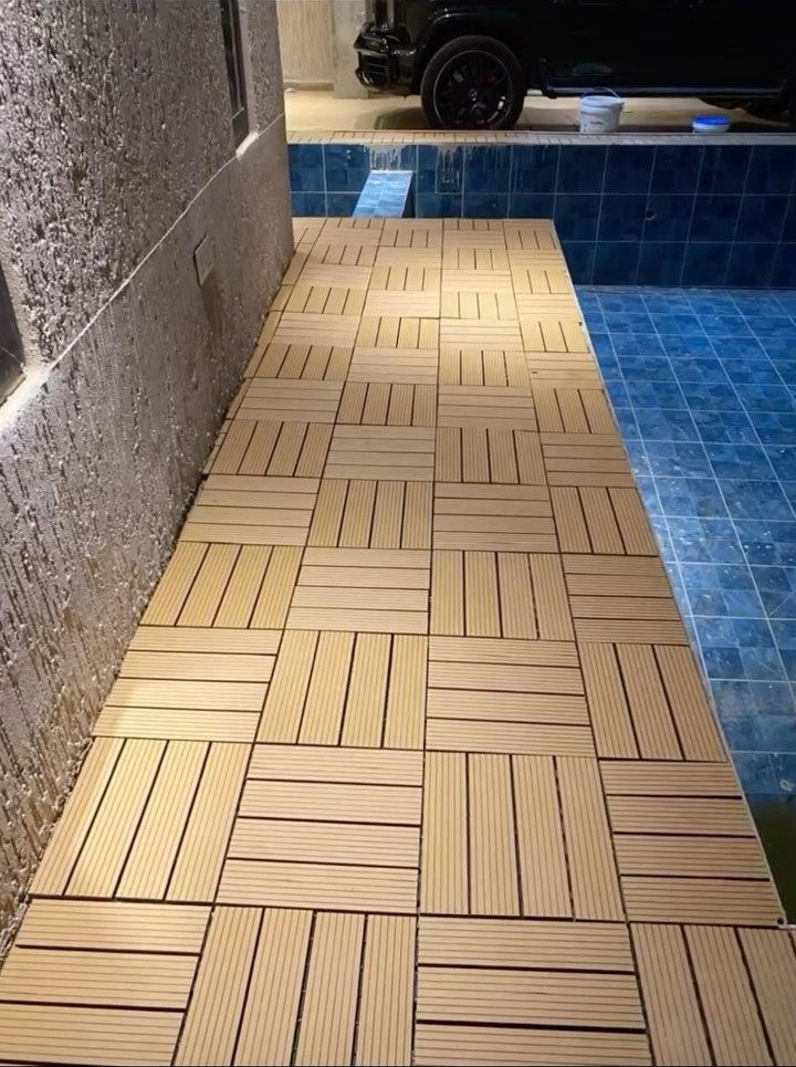 Tan basketweave interlocking tiles installed on a narrow pool deck next to blue water.