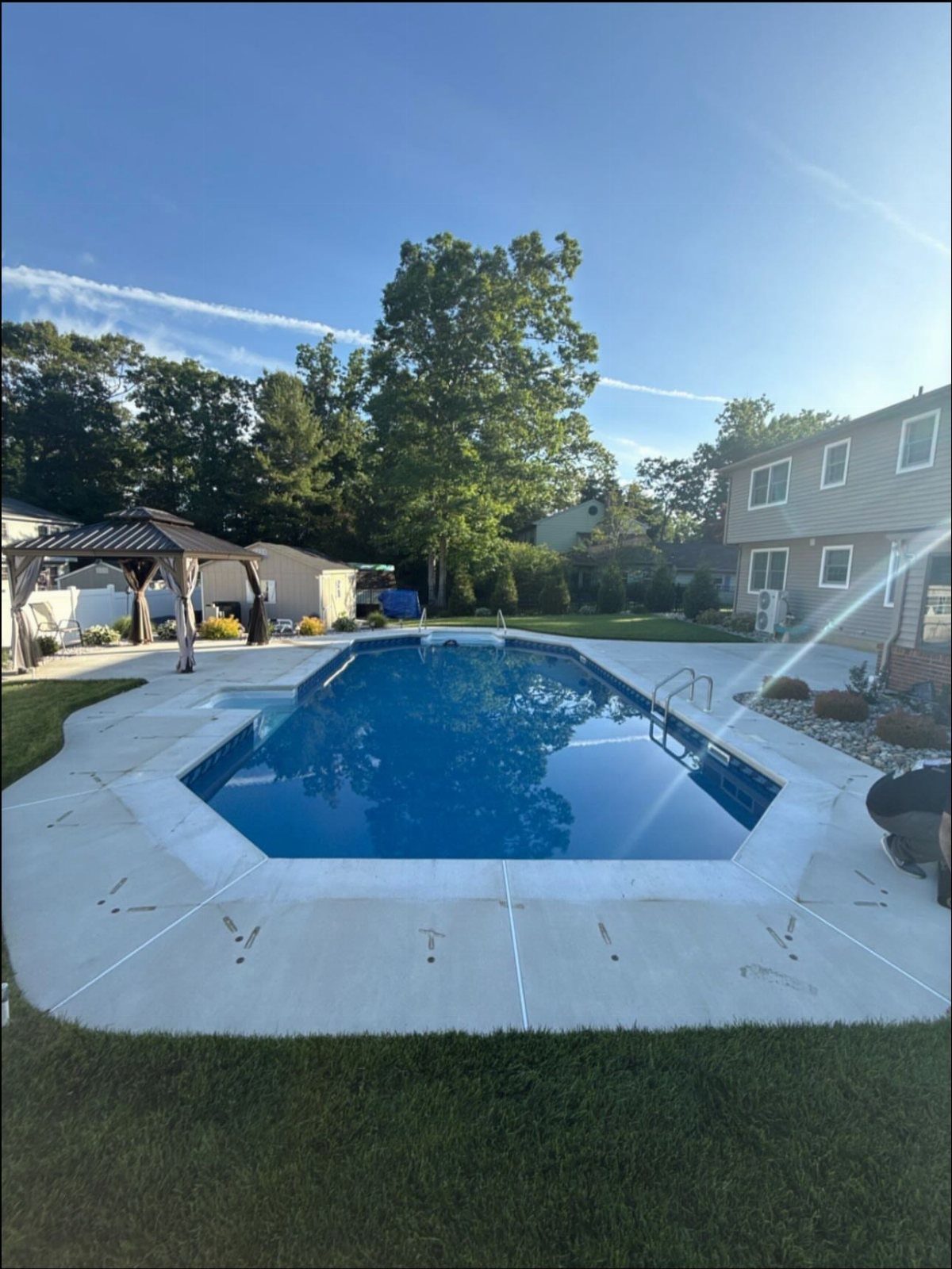 A rectangular blue swimming pool surrounded by a light gray concrete deck in a backyard.