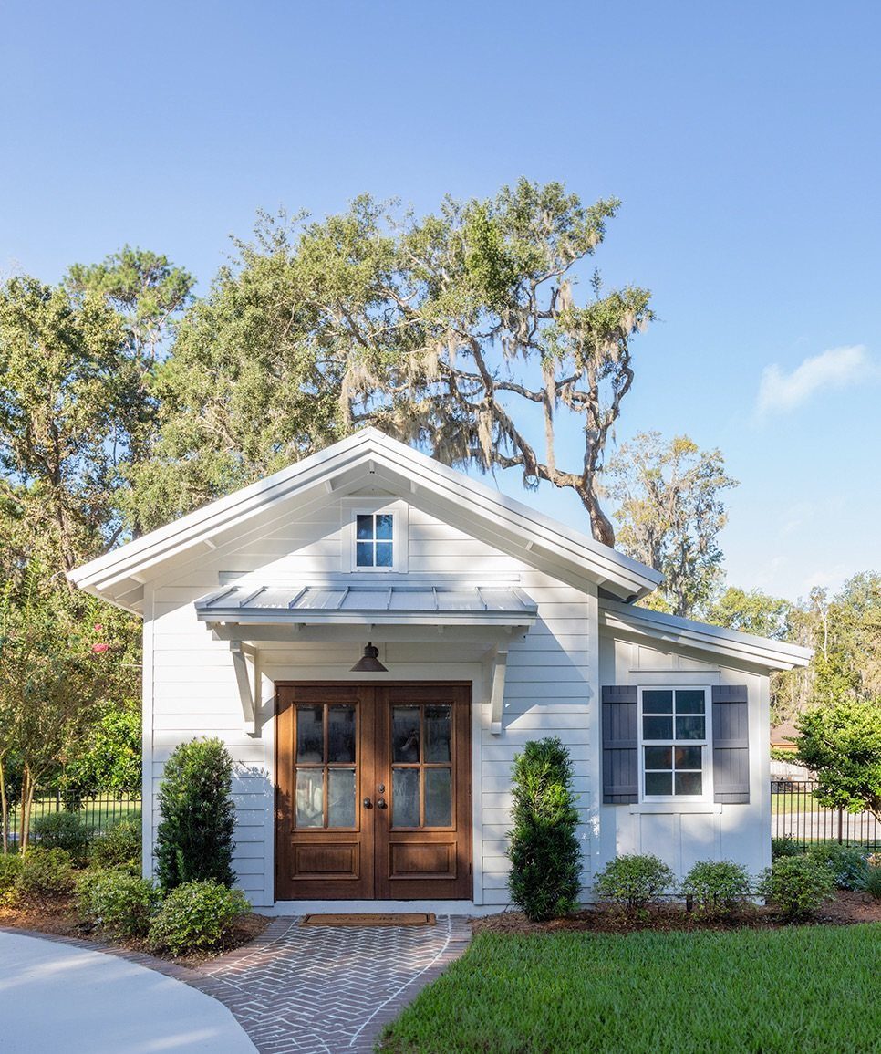 Cottage Garden Sheds with Porch: 13 Layouts and Looks 12 White wooden cottage building with dark wood doors and a small metal porch roof.