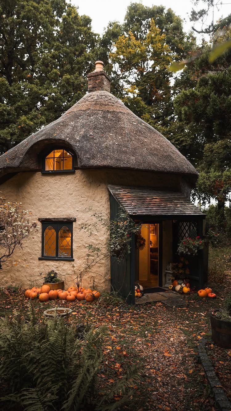 Cottage Garden Sheds with Porch: 13 Layouts and Looks 3 A small round cottage with a thick thatched roof and cream walls nestled among autumn trees.
