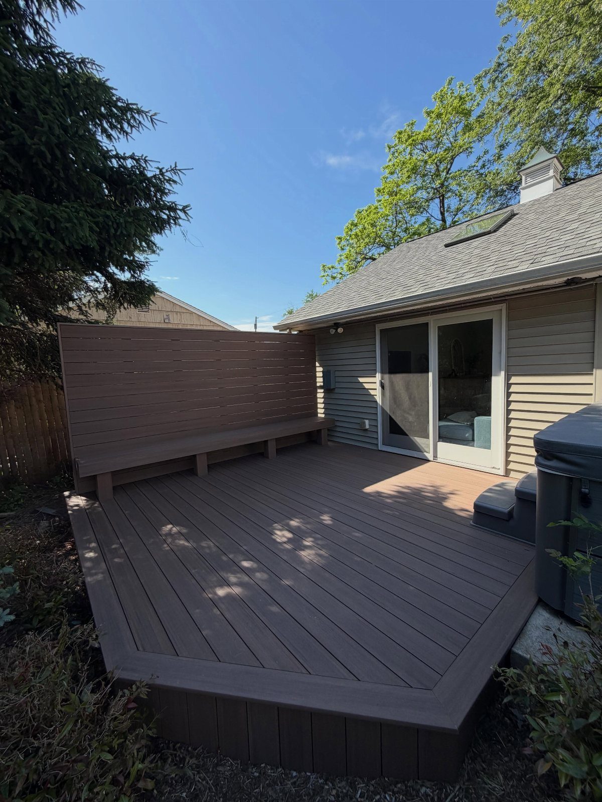 Built-in wooden bench integrated into a horizontal slat privacy wall on a brown composite deck.