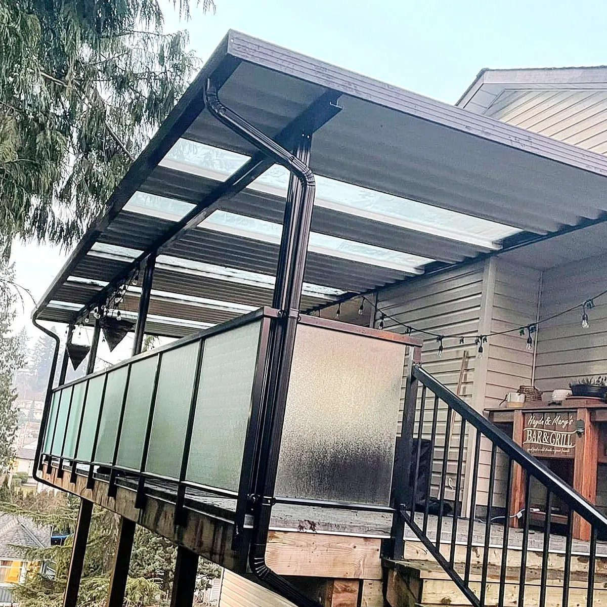 Modern deck with black metal framing, translucent roofing, and frosted glass railing panels.