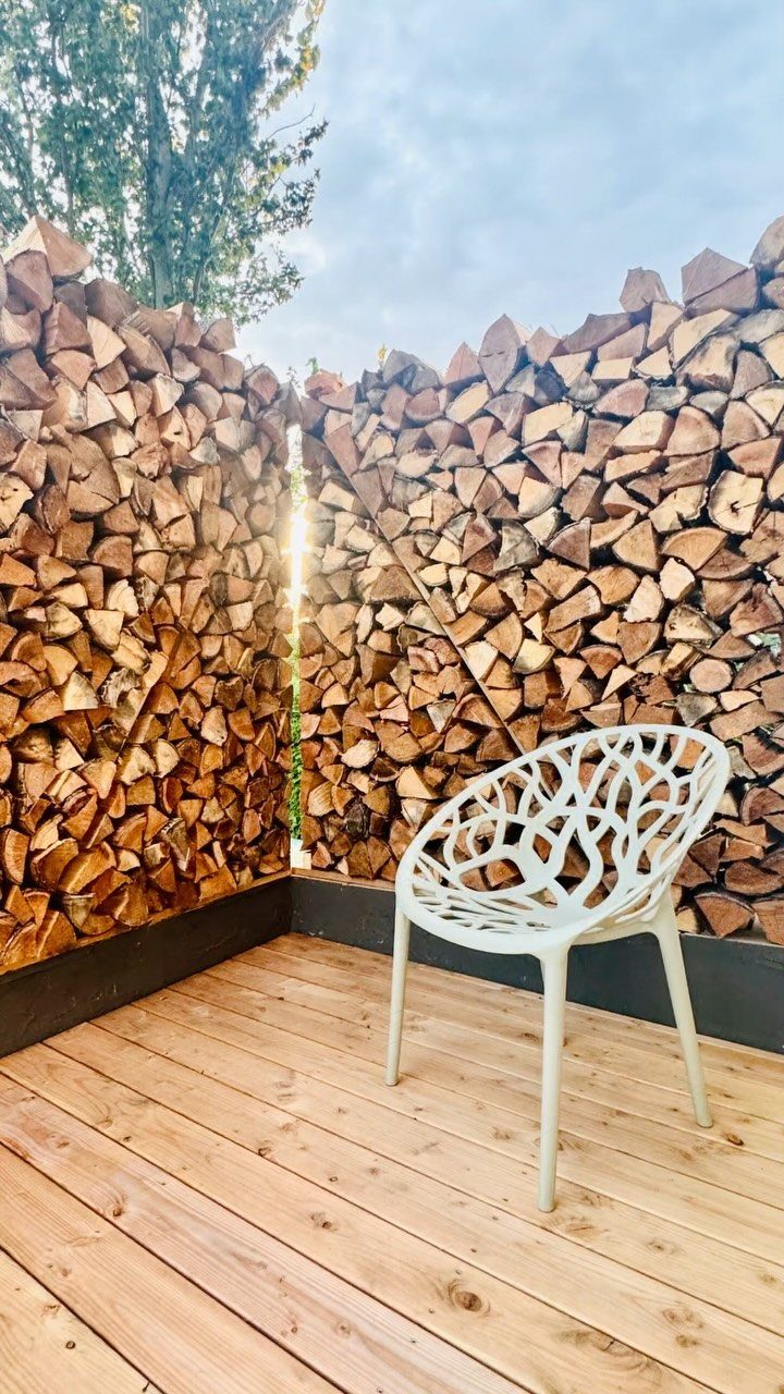 Stacks of split firewood forming privacy walls on a wooden deck with a white chair.