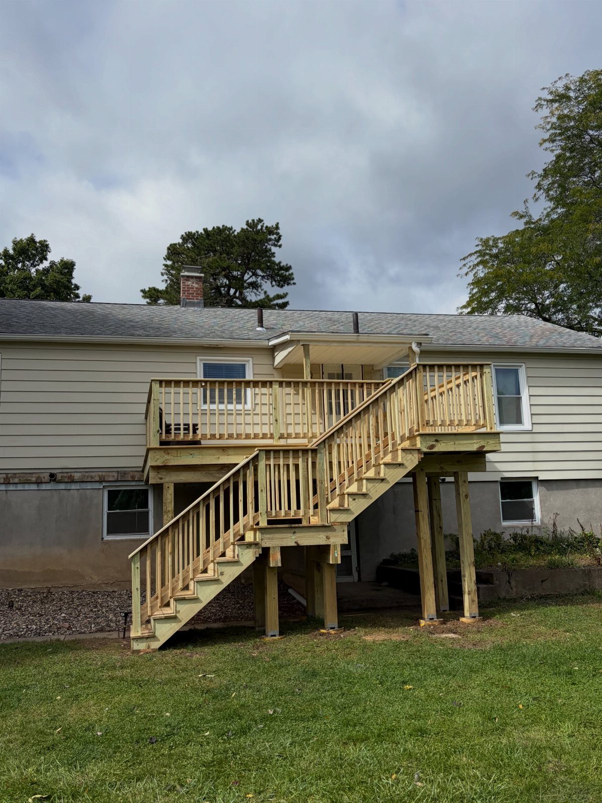 Deck Steps With Landing: 12 Ideas for Any Yard 1 Wooden deck stairs leading to a landing supported by thick wooden posts against a house.