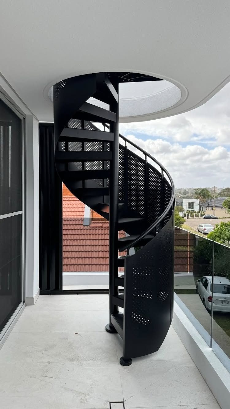 Deck Steps With Landing: 12 Ideas for Any Yard 4 Black metal spiral staircase with perforated steps on a white tiled balcony overlooking a suburban neighborhood.