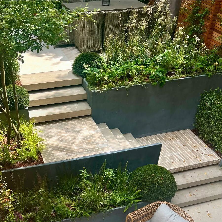 Deck Steps With Landing: 12 Ideas for Any Yard 6 Stone steps integrated with large dark grey planters filled with lush green garden plants.