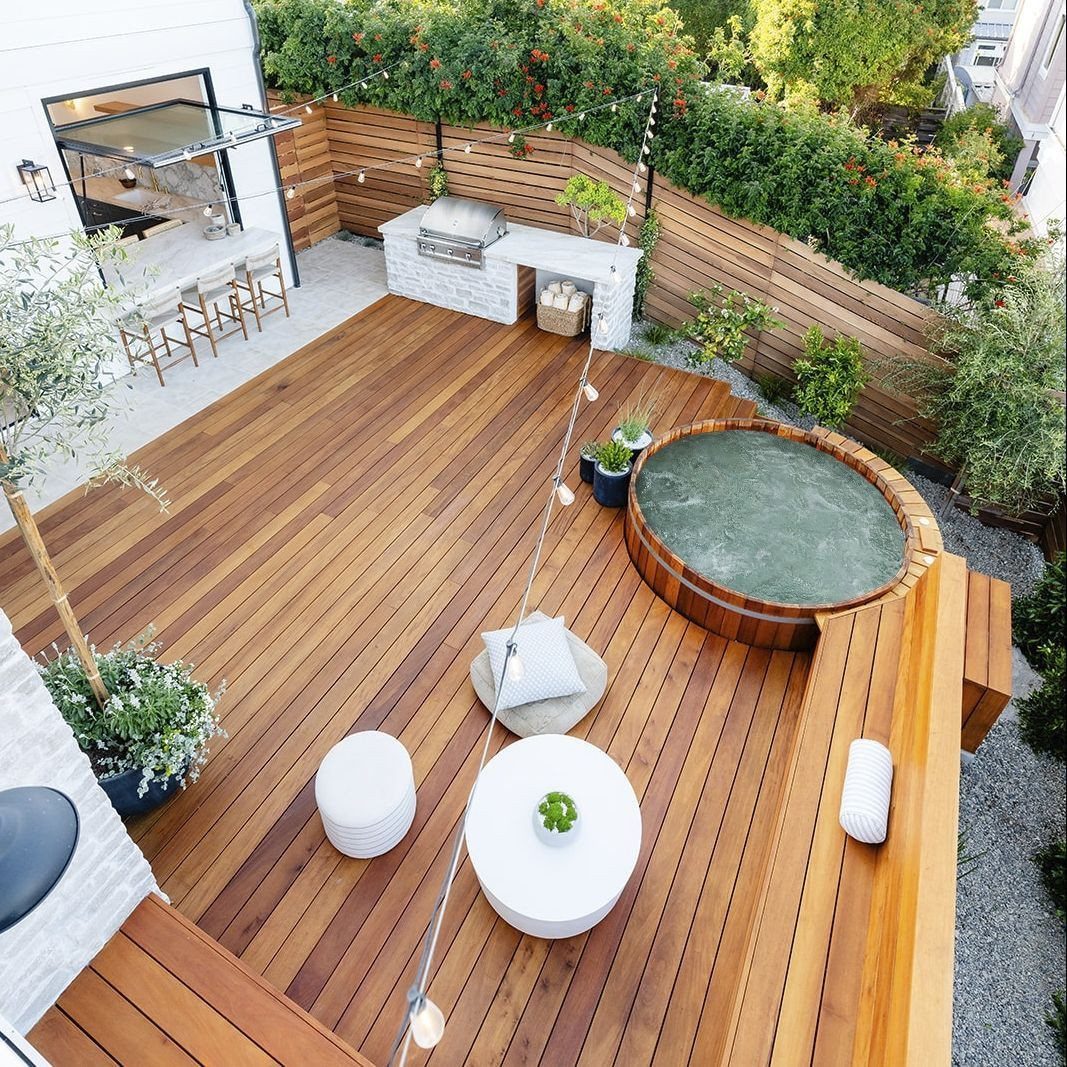 Large wooden deck featuring a circular hot tub, white furniture, and a built-in grill area.