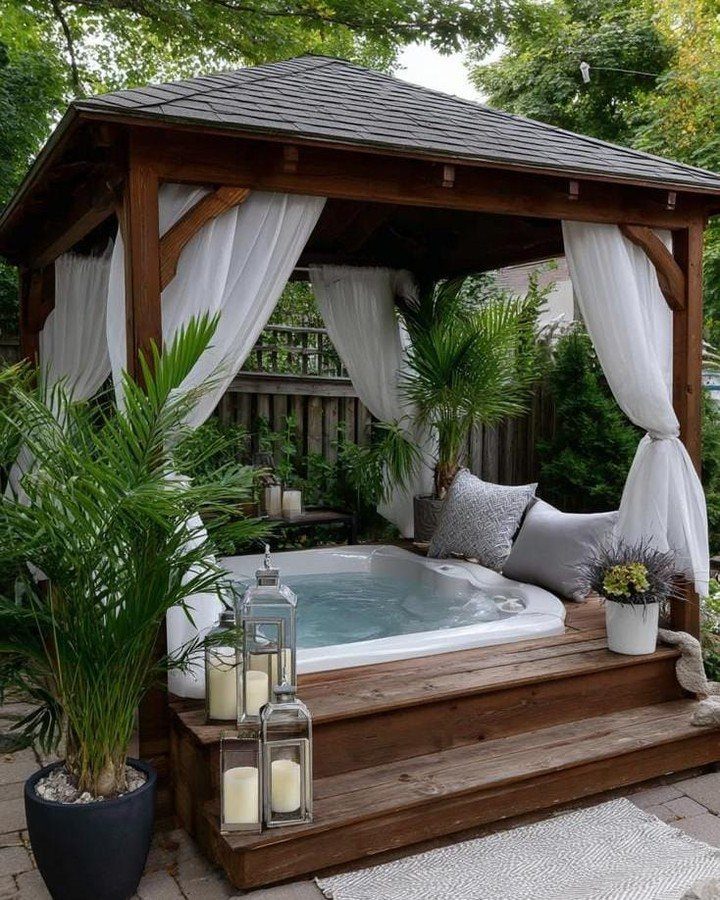 A white hot tub built into a wooden deck under a gazebo with tropical plants.