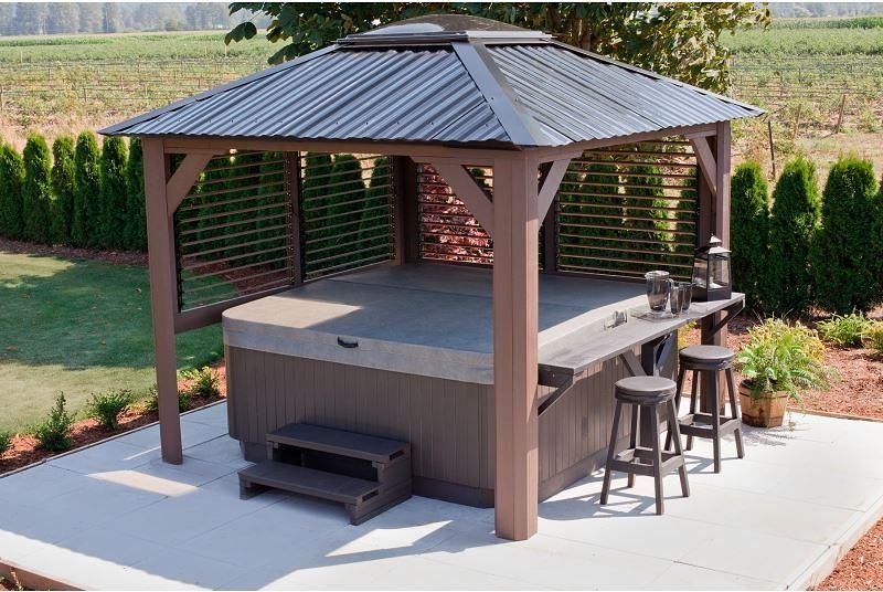 A brown wooden gazebo with a metal roof sheltering a large hot tub and built-in bar.