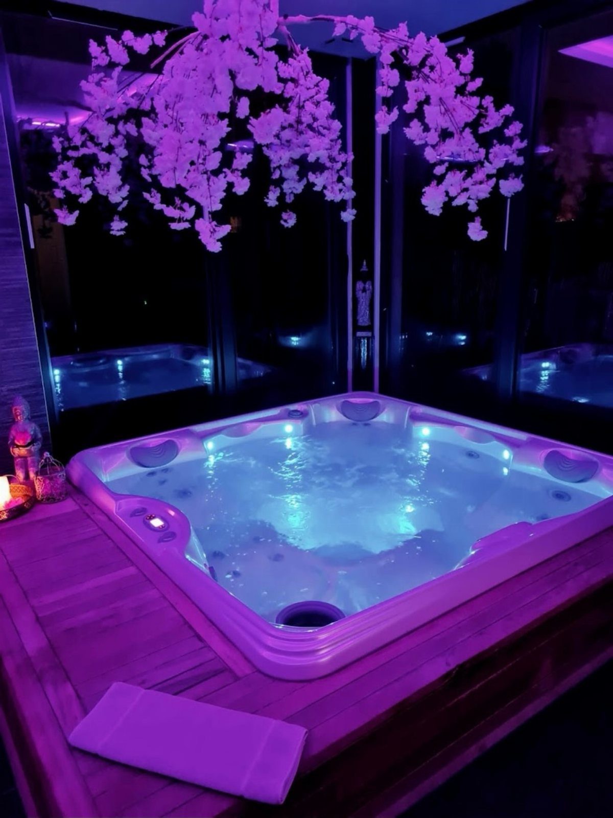 A glowing blue hot tub on a wooden deck under purple lights and white flowers.