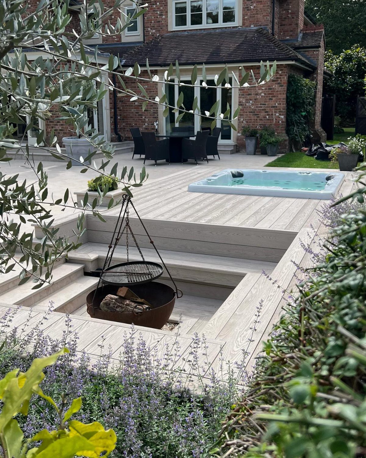 A light grey wooden deck with a sunken hot tub and a fire pit area.