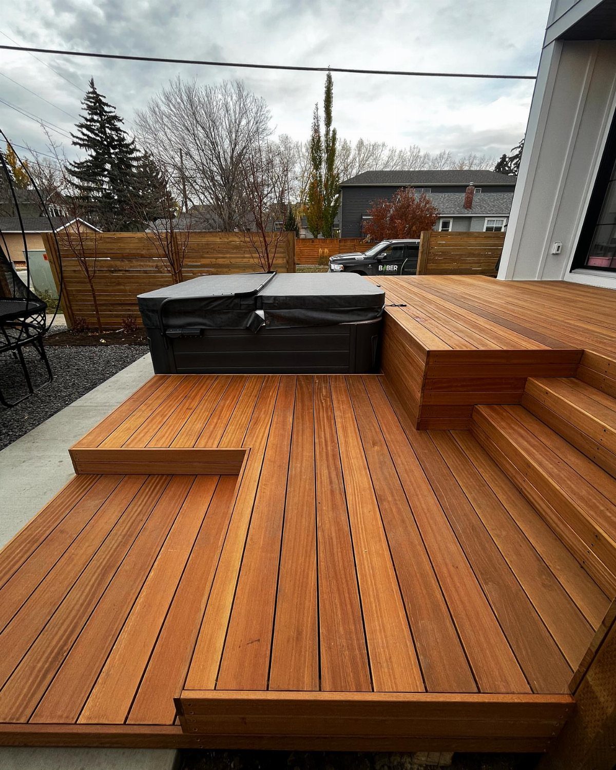 Wooden multi-level deck with a black covered hot tub and wide integrated steps.