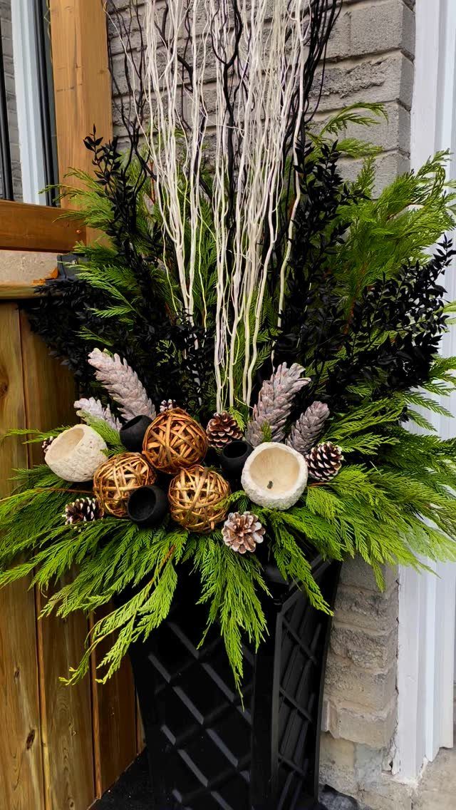 12 Decor for Winter After Christmas Ideas for a Cozy Home 1 Evergreen branches and white birch twigs arranged in a black planter with pinecones and decorative spheres.
