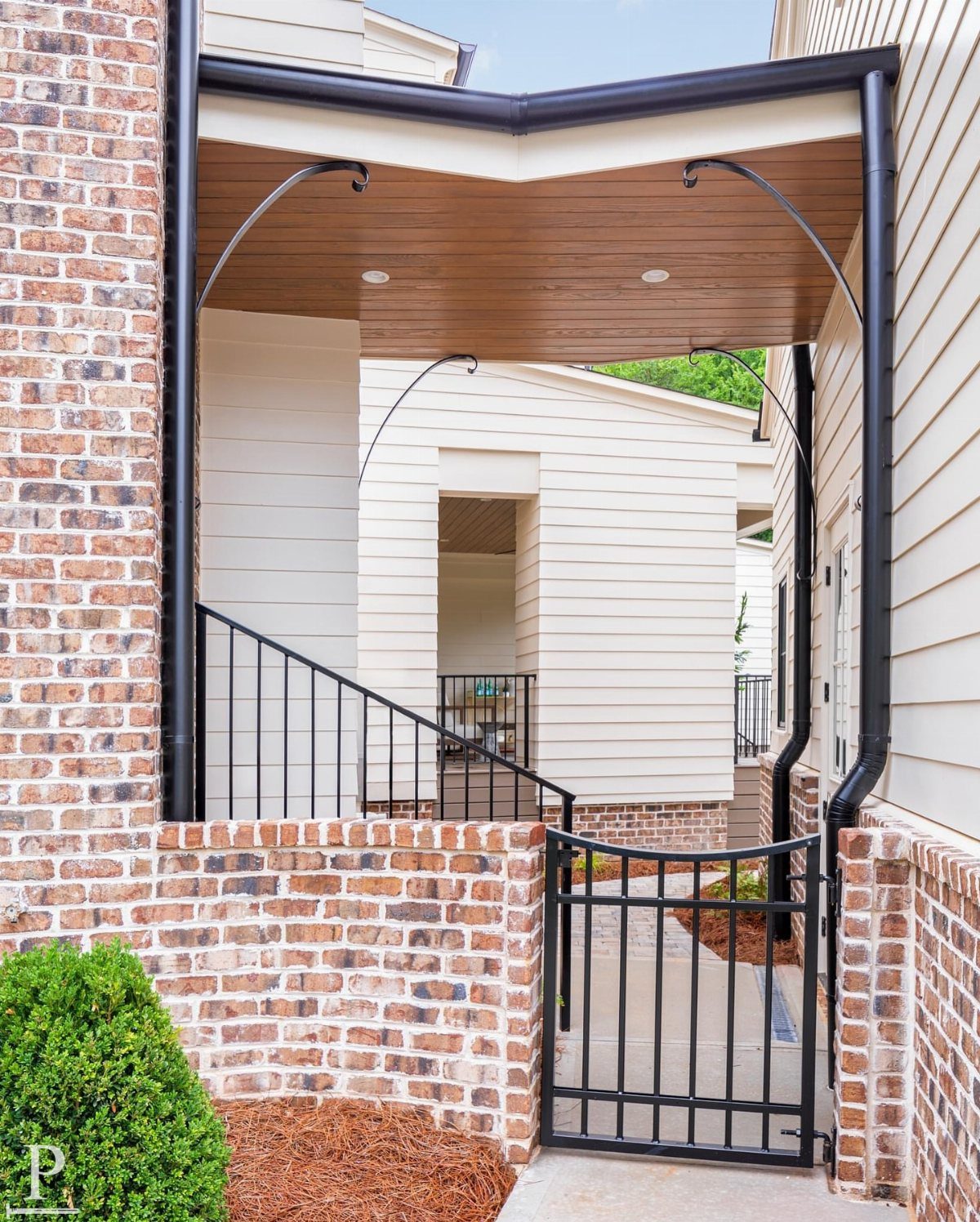 Detached Garage with Breezeway to House: 8 Ideas 8 A covered breezeway with wood ceiling and black metal supports connecting two brick and siding buildings.