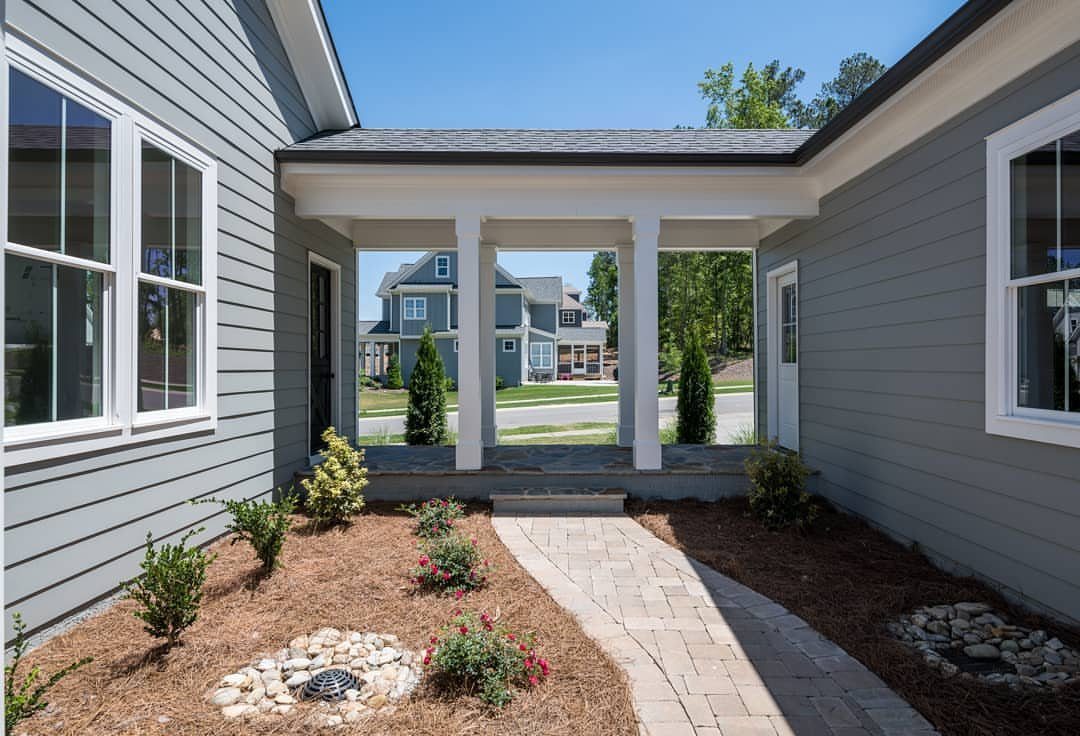 Detached Garage with Breezeway to House: 8 Ideas 4 An open breezeway with white columns connects two gray buildings over a stone walkway.