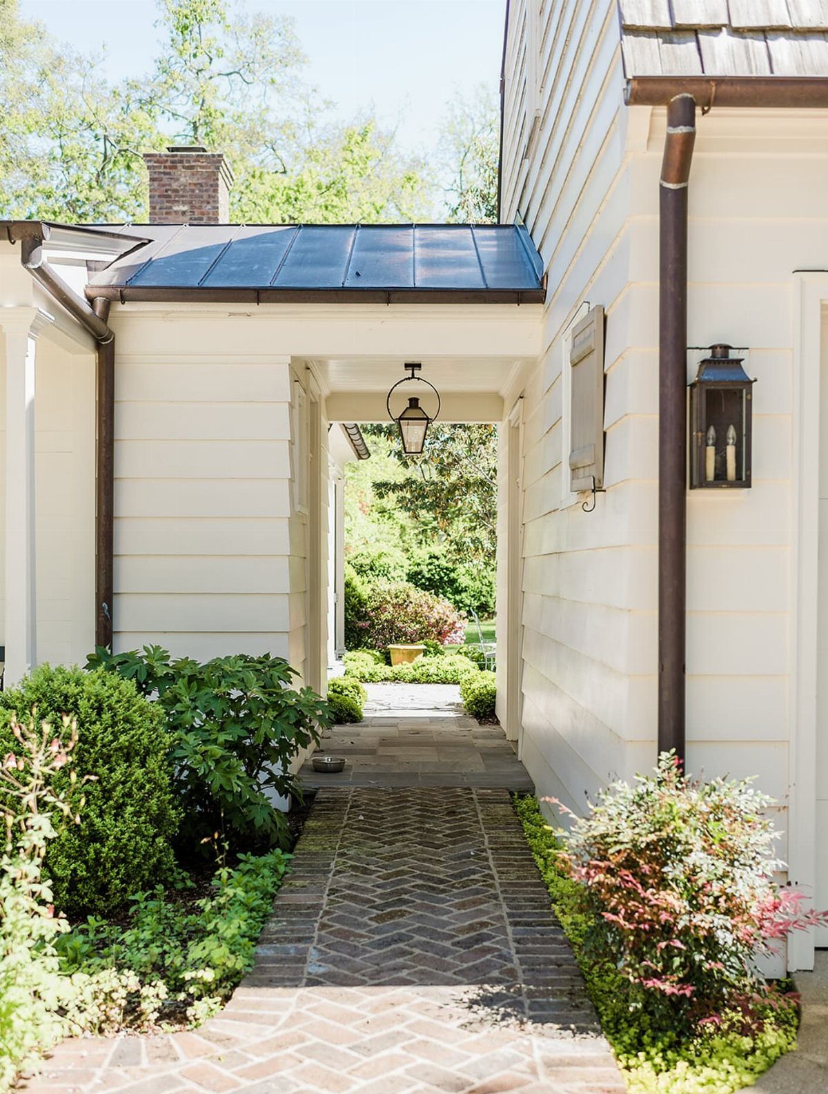 Detached Garage with Breezeway to House: 8 Ideas 1 Brick walkway passing through a covered breezeway between two white houses with green shrubbery.