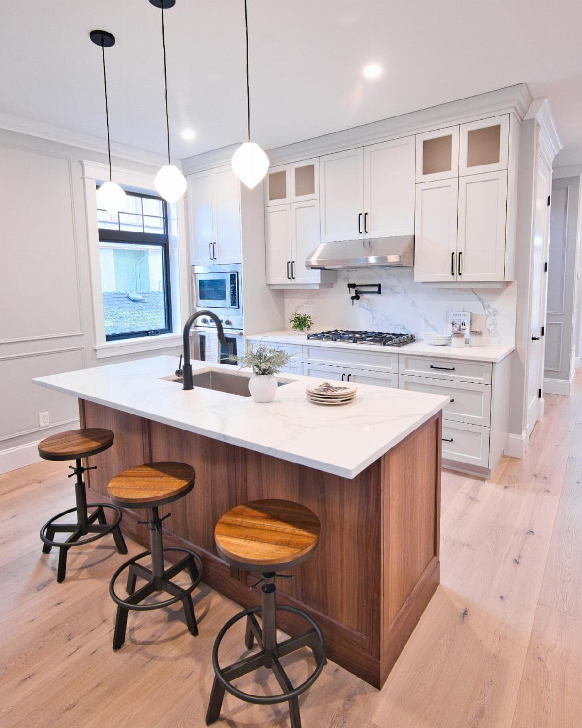 17 DIY Kitchen Island Ideas From Dressers to Live-Edge Slabs 8 A wooden kitchen island with a white marble countertop, built-in sink, and three wooden stools.