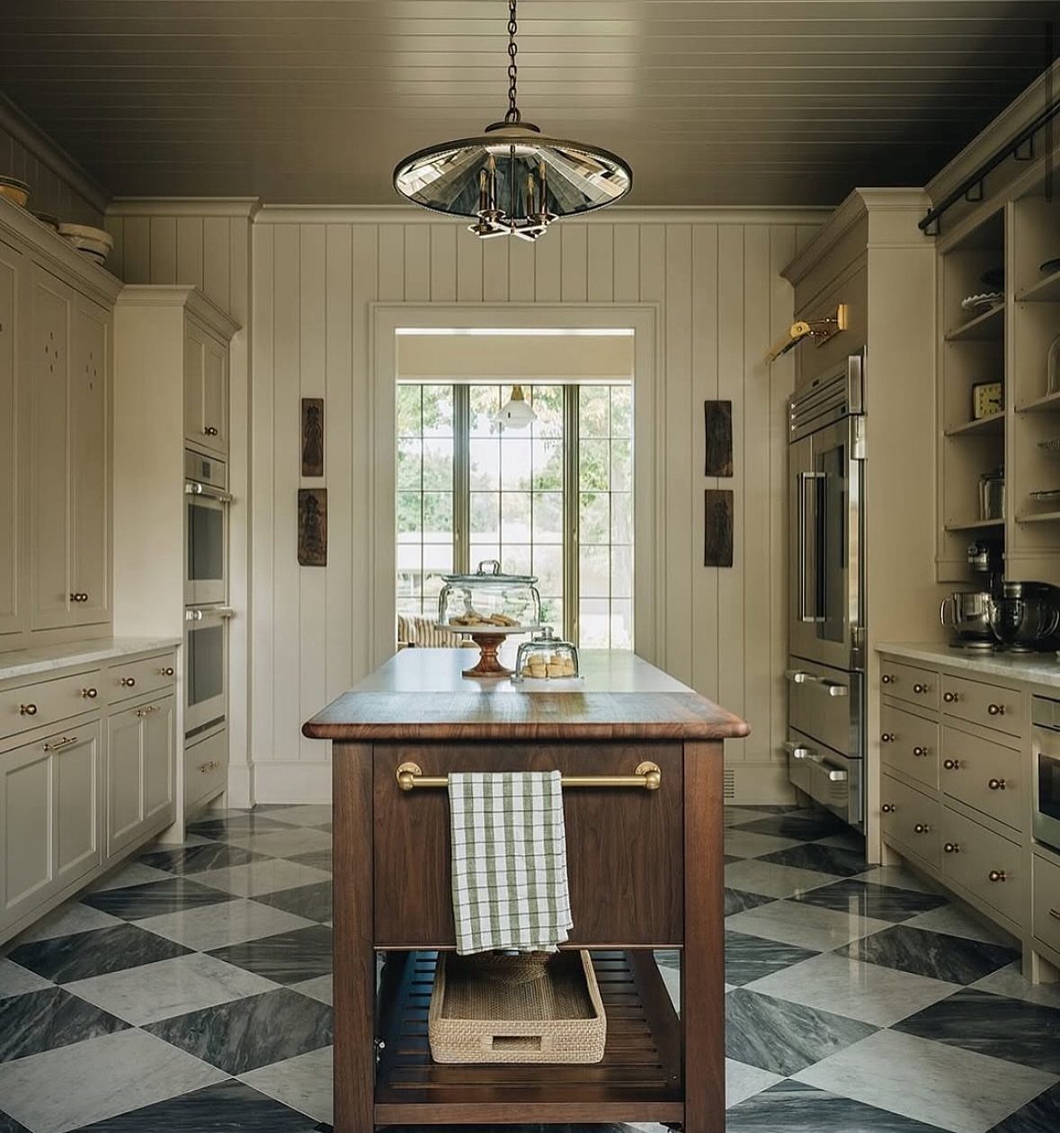 17 DIY Kitchen Island Ideas From Dressers to Live-Edge Slabs 14 A dark wood kitchen island with a towel hanging on a brass rod in a marble floor kitchen.