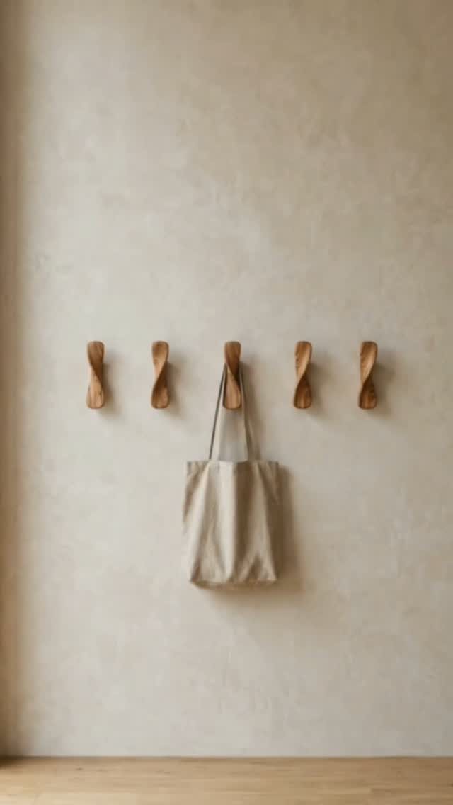 Five twisted wooden wall hooks mounted on a beige textured wall with a tote bag hanging.