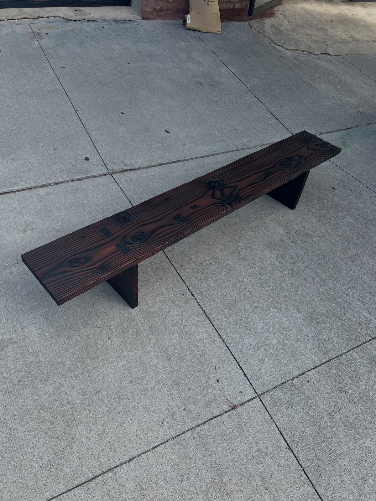 A long dark-stained wooden bench resting on a grey concrete pavement.