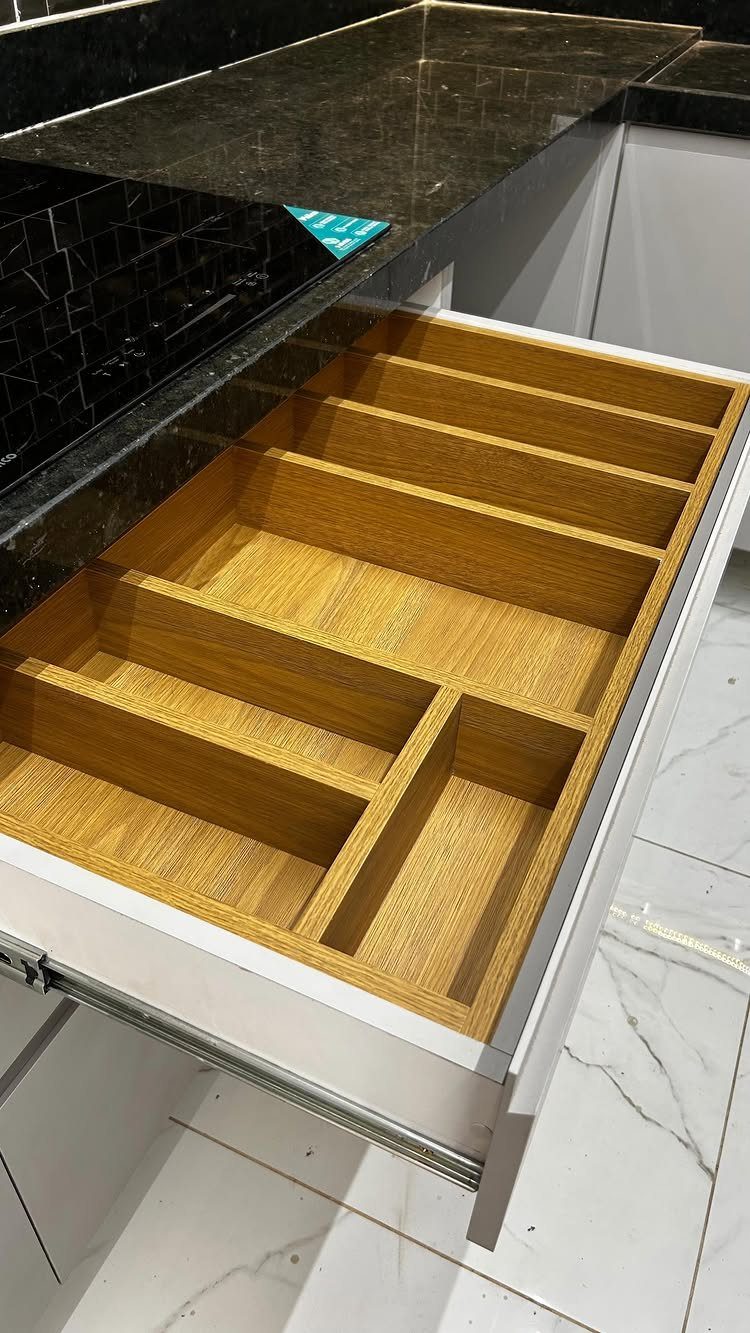 A light wood drawer organizer with multiple compartments inside an open white kitchen drawer.
