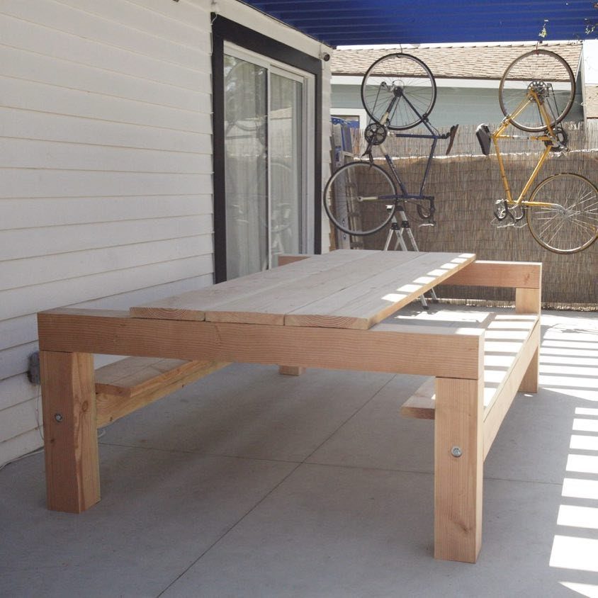 A light wood picnic table with built-in benches on a concrete patio.