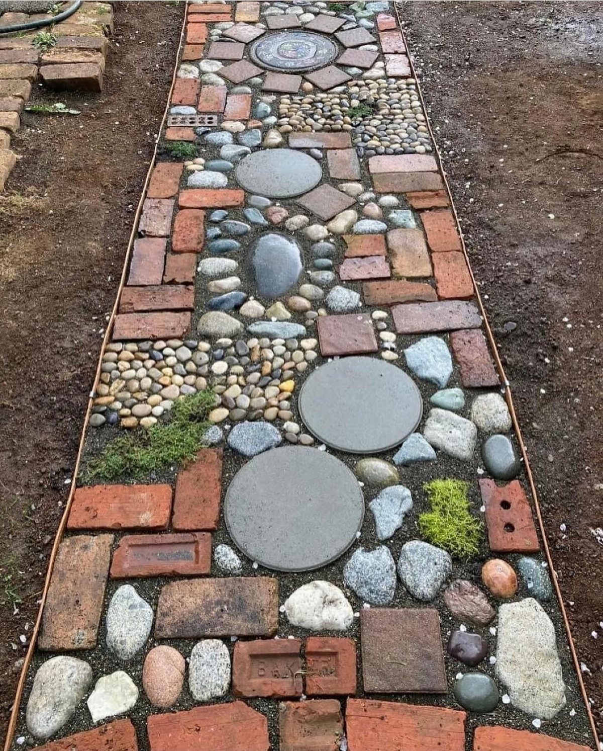 A mosaic garden path composed of red bricks, large circular stones, and small pebbles.