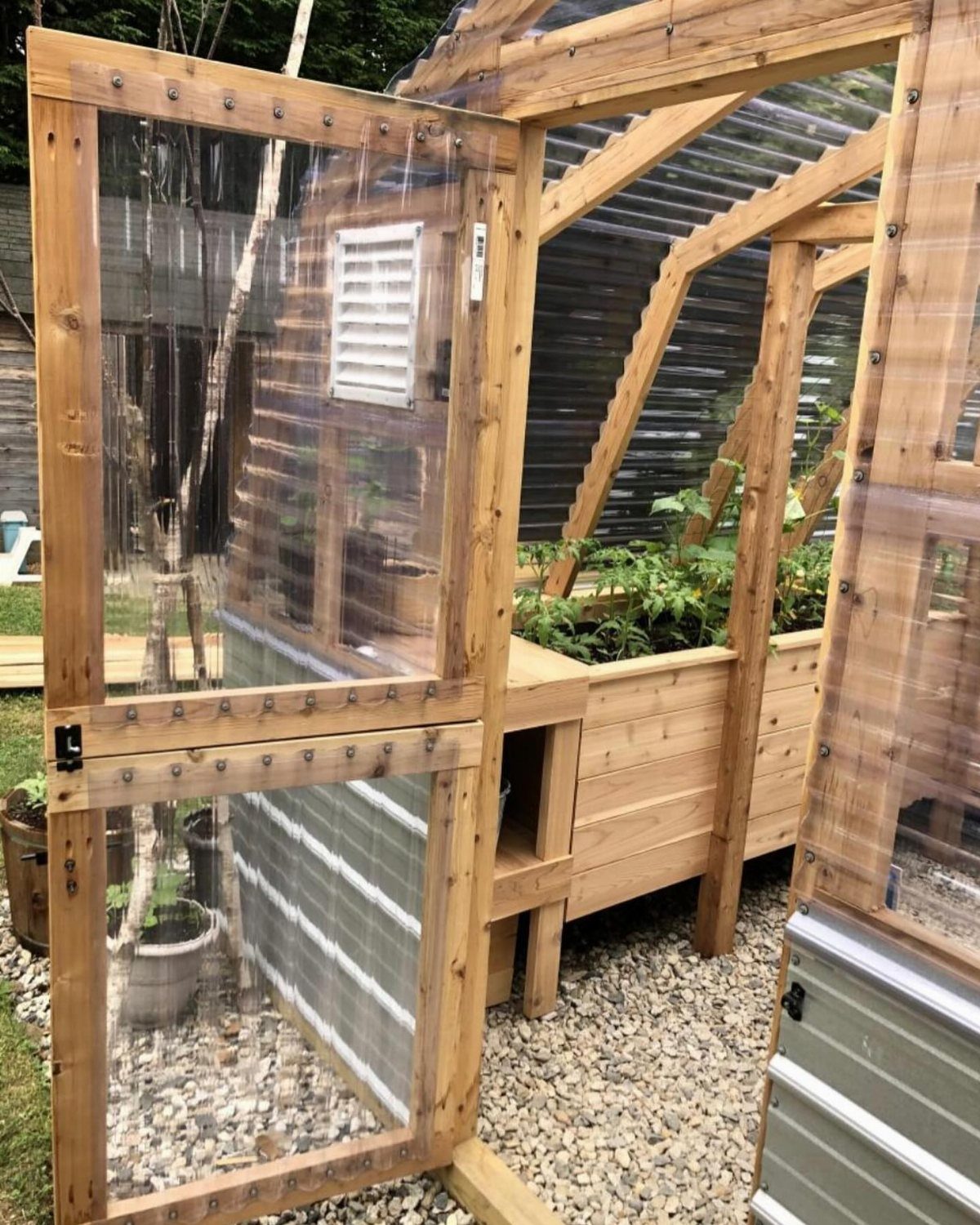 10 Easy Greenhouse Ideas for Any Backyard and Budget 5 A wooden DIY raised garden bed greenhouse with translucent corrugated panels on a gravel ground.