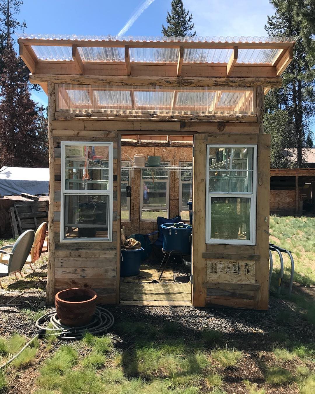 10 Easy Greenhouse Ideas for Any Backyard and Budget 2 A small wooden greenhouse constructed using various reclaimed white-framed windows and a translucent roof.