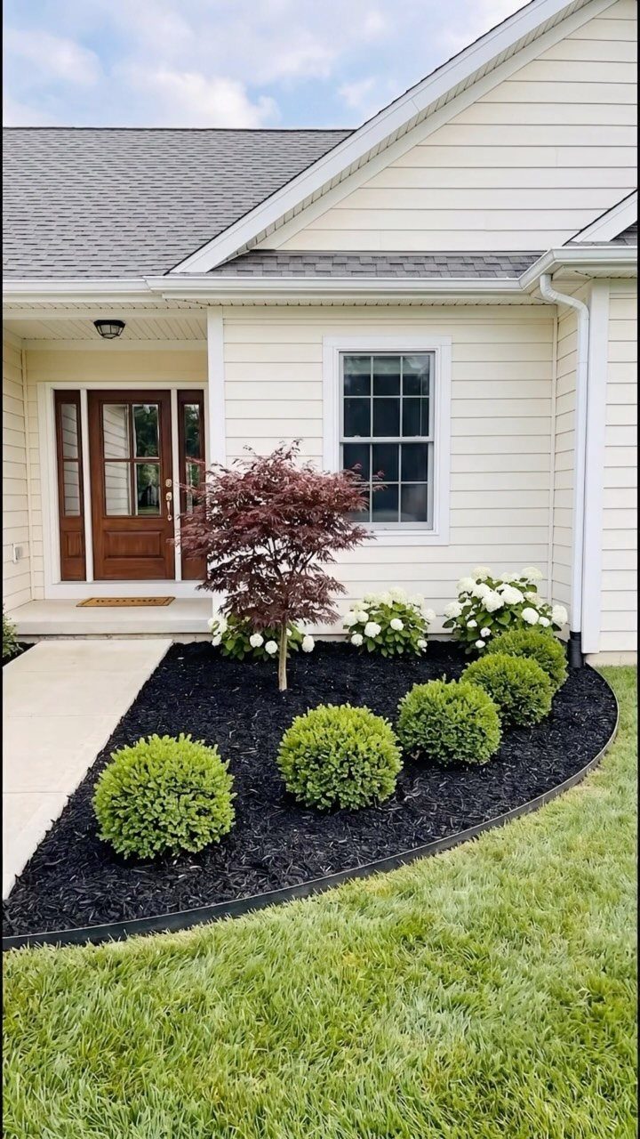 17 Front Flower Bed Ideas for Small Yards and Sunny Corners 15 A landscaped garden bed with green shrubs, white flowers, and a small red maple tree against a house.