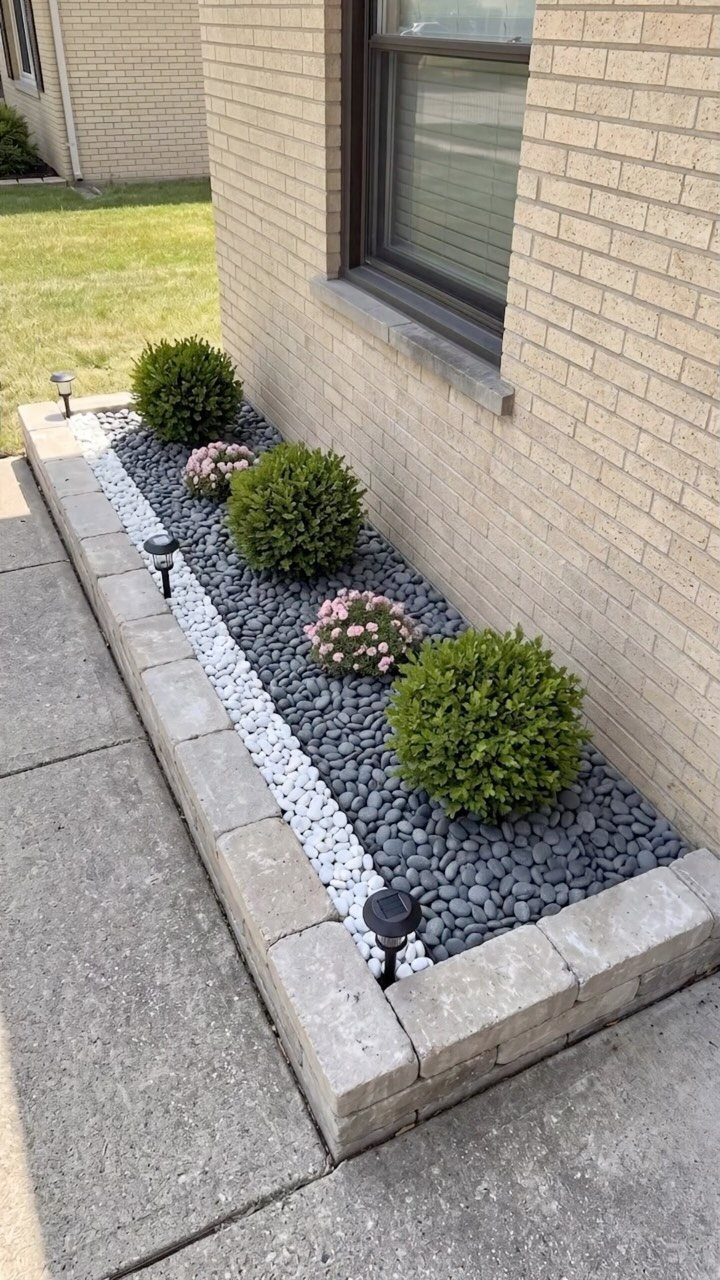 17 Front Flower Bed Ideas for Small Yards and Sunny Corners 17 A landscaped flower bed with green shrubs and pink flowers set in grey and white pebbles.