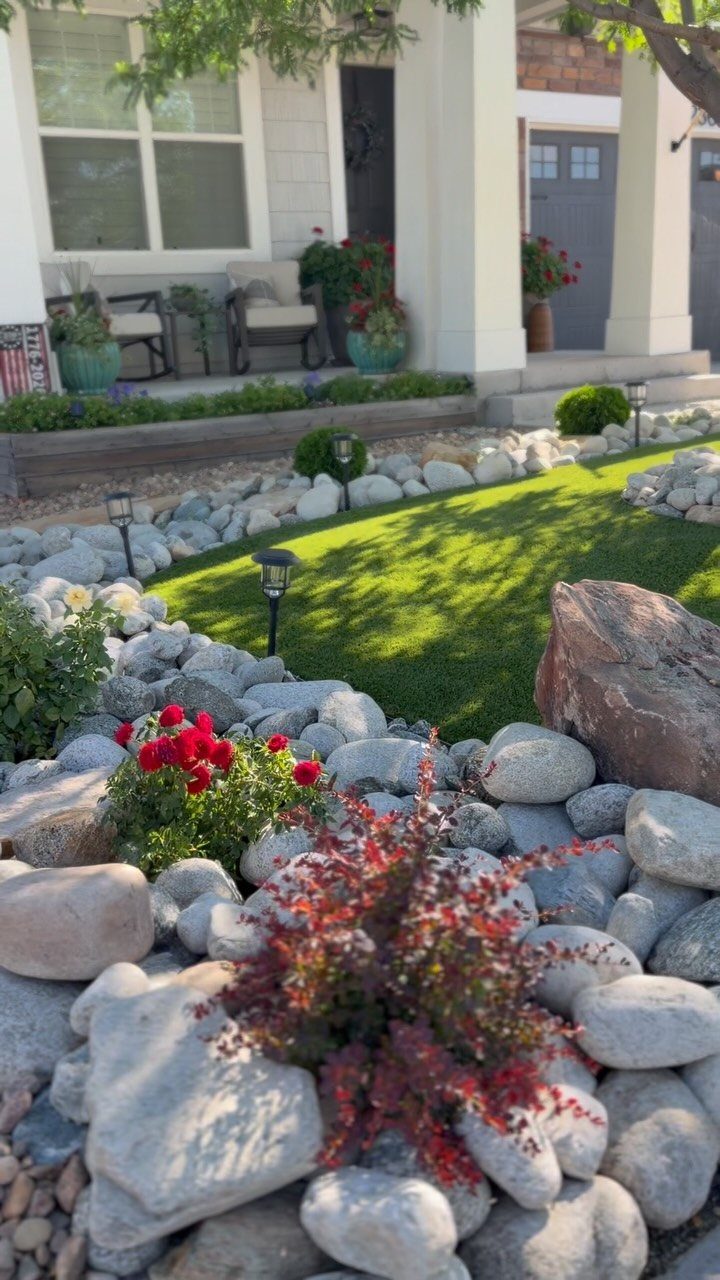 13 Front Lawn Landscaping Ideas for Curb Appeal and Low Upkeep 2 Artificial turf lawn surrounded by large grey rocks, small shrubs, and solar path lights.
