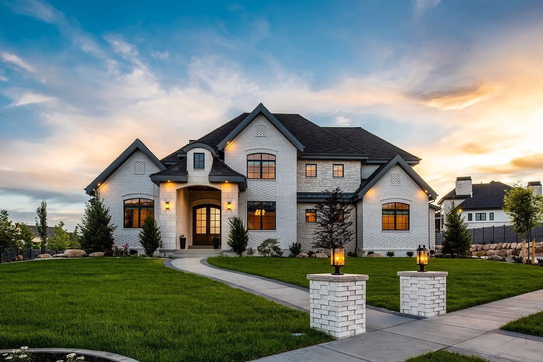 13 Front Lawn Landscaping Ideas for Curb Appeal and Low Upkeep 13 Large white brick house with a green lawn and lit lanterns on brick pillars at sunset.