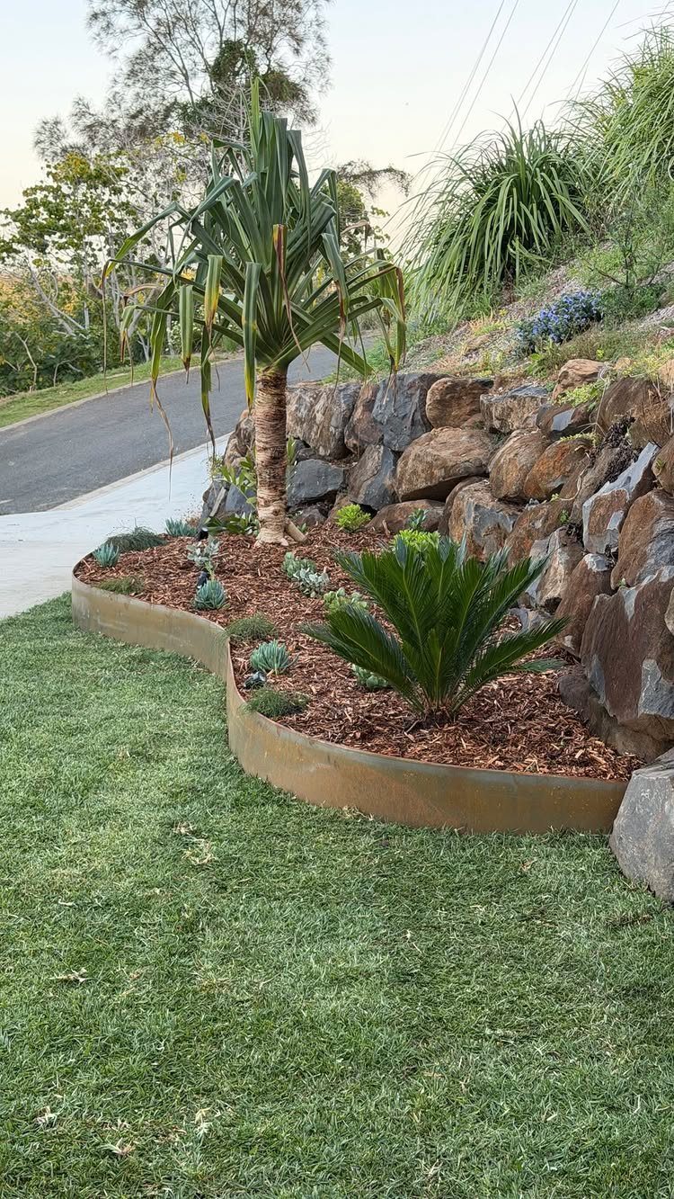 13 Front Lawn Landscaping Ideas for Curb Appeal and Low Upkeep 6 Tropical plants and succulents growing in a mulched garden bed with a stone retaining wall.